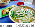 A slightly wider shot of Vietnamese pho with fresh side dishes. Lime and red bowl on a blue plastic table. 143510146