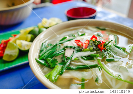 越南炸薯條盛放在藍色的桌子上，配上鮮豔的配料，包括辣椒、青檸片和新鮮香草。 143510149