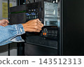 A technician wearing denim sleeve works both hands inside an open server rack stacked drive bays metal panels cables visible close view of computer equipment maintenance 143512313