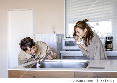 一位帶著嬰兒的家庭主婦在廚房水龍頭維修後向水電工詢問狀況。 一位帶著嬰兒的家庭主婦在廚房水龍頭維修後向水電工詢問狀況。 143513093