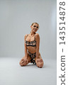 Blonde woman in geometric mesh lingerie kneeling in studio 143514878