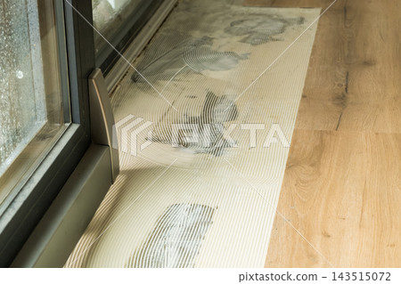 On a clean vinyl floor, sticky adhesive marks are being meticulously removed near a bright glass sliding door, showing the maintenance of interior surfaces. 143515072