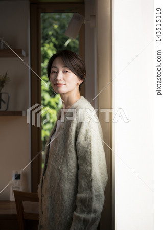 一幅日本女性的肖像畫,她站在自家窗邊,沐浴在自然光中,身穿秋冬針織衫和開襟衫。 一幅日本女性的肖像畫,她站在自家窗邊,沐浴在自然光中,身穿秋冬針織衫和開襟衫。 143515119
