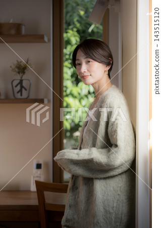 一幅日本女性的肖像畫,她站在自家窗邊,沐浴在自然光中,身穿秋冬針織衫和開襟衫。 一幅日本女性的肖像畫,她站在自家窗邊,沐浴在自然光中,身穿秋冬針織衫和開襟衫。 143515120