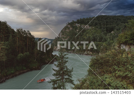 Motorboat sailing on Katun River through mountain valley under dramatic sky Motorboat sailing on Katun River through mountain valley under dramatic sky 143515403