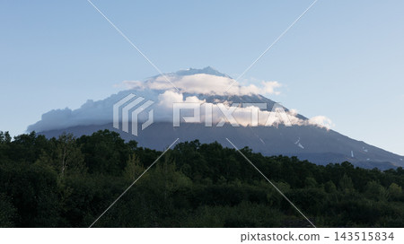 Majestic volcanic peak covered in soft white clouds above dense green forest Majestic volcanic peak covered in soft white clouds above dense green forest 143515834