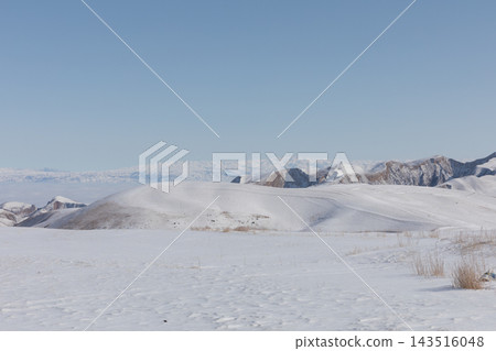Snow covered rolling hills and mountain ridges under clear blue sky Snow covered rolling hills and mountain ridges under clear blue sky 143516048