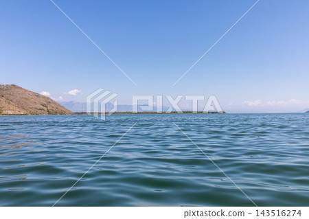 Scenic view across calm blue water ripples at Lake Skadar with distant mountains Scenic view across calm blue water ripples at Lake Skadar with distant mountains 143516274
