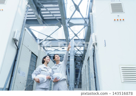 兩名年輕的日本男子和女子,其中一人戴著安全帽,正在進行建築物維護工作。 兩名年輕的日本男子和女子,其中一人戴著安全帽,正在進行建築物維護工作。 143516878