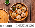 Steam basket with dumplings served with dipping sauce on a wooden table 143519120