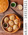 Steam basket with dumplings served with dipping sauce on a wooden table 143519121