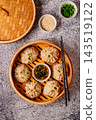 Steamed dumplings served in a bamboo basket with dipping sauce 143519122