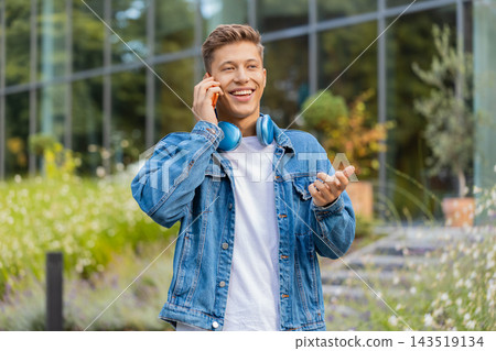 Young man talking on phone during call walking in city street with friendly relaxed smile outdoors Young man talking on phone during call walking in city street with friendly relaxed smile outdoors 143519134
