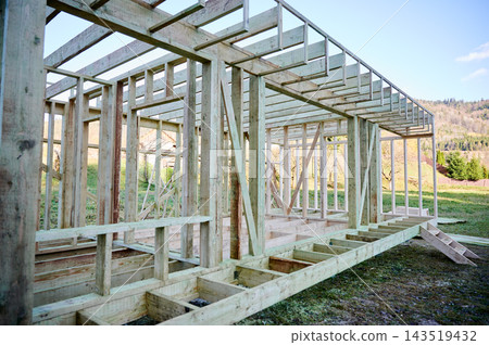 Timber frame house under construction in countryside, unfinished wooden structure Timber frame house under construction in countryside, unfinished wooden structure 143519432