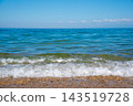 The clear blue sea and white waves crashing against the sandy beach 143519728