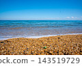 A landscape of a pebble beach with a blue sky and calm sea. 143519729