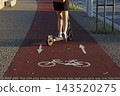 Electric scooter traveling along a dedicated cycling path marked with bicycle symbols and directional arrows, urban micromobility, road safety, shared routes, and modern city infrastructure. 143520275