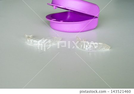 Clear dental aligner trays with purple case close up. Close up of transparent dental aligner trays displayed with purple orthodontic storage case, clear dental appliance and organized carrying solutio 143521460