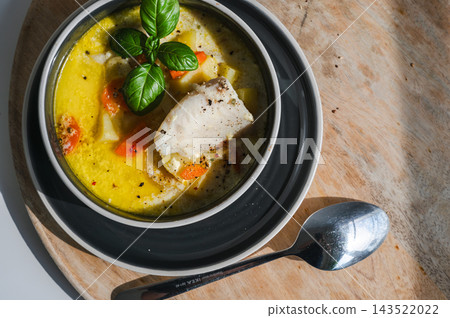 Belgian Waterzooi With a White Fish Fillet From Above. Overhead view of Belgian waterzooi with a fillet of white fish, carrot and potato in a creamy broth, served in layered bowls with fresh basil and Belgian Waterzooi With a White Fish Fillet From Above. Overhead view of Belgian waterzooi with a fillet of white fish, carrot and potato in a creamy broth, served in layered bowls with fresh basil and 143522022