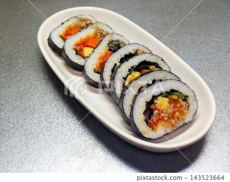 韓式紫菜包飯(一種餡料豐富的韓式海苔捲)擺放在長長的白色盤子上。 韓式紫菜包飯(一種餡料豐富的韓式海苔捲)擺放在長長的白色盤子上。 143523664