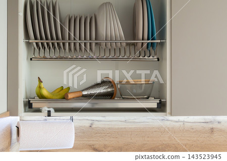 Plates and kitchen tools are arranged in a cupboard. Bananas sit on a shelf next to a bowl and a grater Plates and kitchen tools are arranged in a cupboard. Bananas sit on a shelf next to a bowl and a grater 143523945