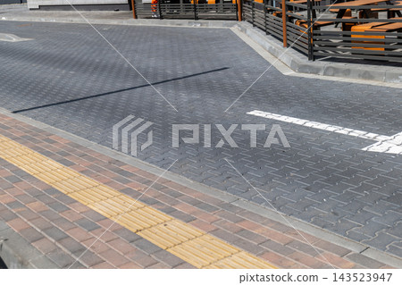 A road intersection shows a textured pavement and a clear pedestrian path. The setting is in an urban area with nearby structures 143523947