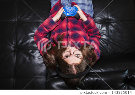 Teenage Girl Playing Upside Down on the Couch. A playful teenage girl lies upside down on the couch holding her game controller while playing a video game at home. Teenage Girl Playing Upside Down on the Couch. A playful teenage girl lies upside down on the couch holding her game controller while playing a video game at home. 143525014