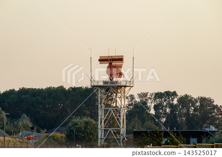 Airport Radar Tower Against the Treeline. An airport radar tower stands against the treeline at Brussels Airport in Belgium, the surveillance antenna used to track aircraft movements. 143525017