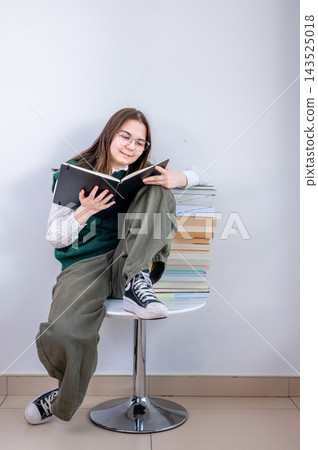 Teen Girl Pointing at Book as Peer Tutor with Study Materials. Enthusiastic teenage girl pointing at open book while presenting study materials as peer tutor. Friendly approachable smile with stack of Teen Girl Pointing at Book as Peer Tutor with Study Materials. Enthusiastic teenage girl pointing at open book while presenting study materials as peer tutor. Friendly approachable smile with stack of 143525018