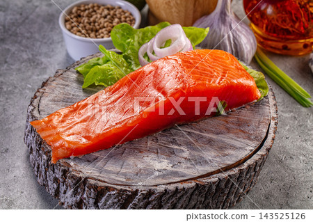 Wooden cutting board with raw salmon fillet, fresh lettuce, sliced onion, garlic bulb, peppercorns, and saffron oil, seafood preparation Wooden cutting board with raw salmon fillet, fresh lettuce, sliced onion, garlic bulb, peppercorns, and saffron oil, seafood preparation 143525126