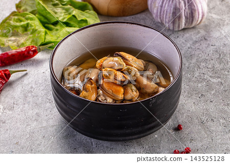 Grey stone surface black ceramic bowl containing cooked orange mussels in clear broth seafood appetizer Grey stone surface black ceramic bowl containing cooked orange mussels in clear broth seafood appetizer 143525128