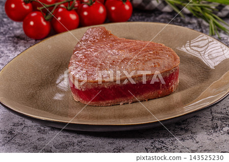 Seared tuna tataki steak with pink rare center on rustic ceramic plate, cherry tomatoes and rosemary nearby, gourmet seafood dish Seared tuna tataki steak with pink rare center on rustic ceramic plate, cherry tomatoes and rosemary nearby, gourmet seafood dish 143525230