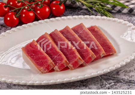 White ceramic plate with beaded rim holding sliced seared tuna tataki with cherry tomatoes and rosemary on stone surface White ceramic plate with beaded rim holding sliced seared tuna tataki with cherry tomatoes and rosemary on stone surface 143525231