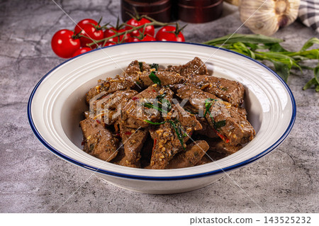 White enamel bowl with blue rim filled with fried beef liver slices garnished with holy basil and chili pepper on gray stone table White enamel bowl with blue rim filled with fried beef liver slices garnished with holy basil and chili pepper on gray stone table 143525232