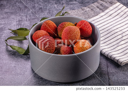 Bowl of lychee fruits with red textured rind arranged in grey ceramic container with striped kitchen towel on dark textured table surface Bowl of lychee fruits with red textured rind arranged in grey ceramic container with striped kitchen towel on dark textured table surface 143525233