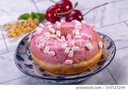 Pink glazed donut topped with mini marshmallows on blue patterned ceramic plate with fresh cherries and white currants in background, sweet pastry dessert Pink glazed donut topped with mini marshmallows on blue patterned ceramic plate with fresh cherries and white currants in background, sweet pastry dessert 143525294