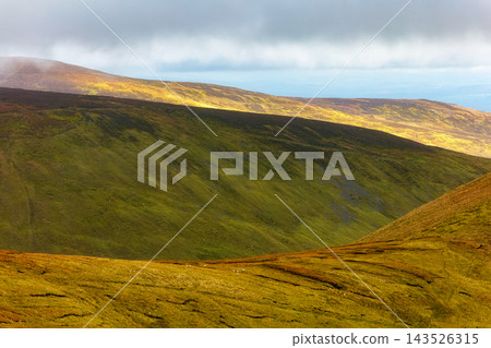 Green, moss-covered hills under a cloudy, shifting Irish sky. 143526315