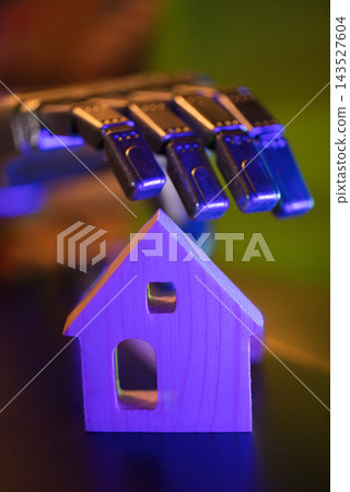 Colorful harmonica resting above a small wooden house model with vivid purple and blue lighting, closeup view of an abstract musical object and miniature shelter 143527604