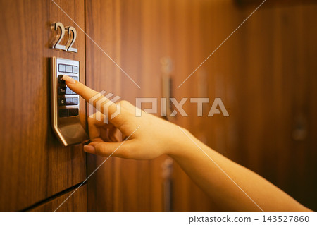Hand pressing keypad on a secure locker with number 22 visible, wooden locker background, indicating a storage or security system in a modern facility Hand pressing keypad on a secure locker with number 22 visible, wooden locker background, indicating a storage or security system in a modern facility 143527860