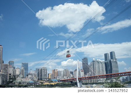 Cable car traveling over a cityscape with modern skyscrapers and a bridge under a blue sky with fluffy clouds in Chongqing, China Cable car traveling over a cityscape with modern skyscrapers and a bridge under a blue sky with fluffy clouds in Chongqing, China 143527952