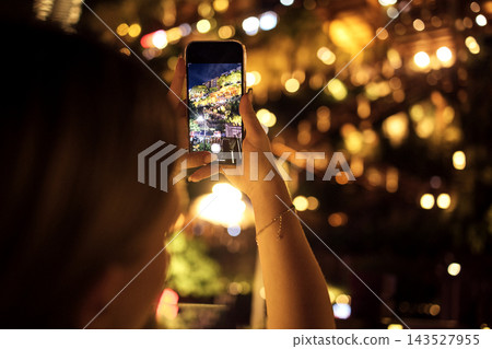 Woman holding smartphone capturing illuminated cityscape at night, colorful lights and blurred background creating a vibrant urban atmosphere 143527955