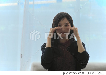 一位年輕女子站在窗邊,用手摀著眼睛,臉上露出淚痕(表達悲傷、震驚、淚水和痛苦)。 一位年輕女子站在窗邊,用手摀著眼睛,臉上露出淚痕(表達悲傷、震驚、淚水和痛苦)。 143528245