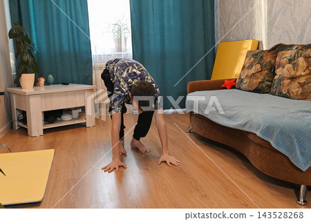 A young man with long hair does yoga at home. Teenager sits in lotus position on the room. Copy space. Place for text A young man with long hair does yoga at home. Teenager sits in lotus position on the room. Copy space. Place for text 143528268