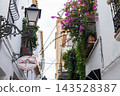 Charming Altea street showcases whitewashed buildings adorned with vibrant bougainvillea, a classic street lamp, and inviting eateries, perfect for Spanish family holidays 143528387