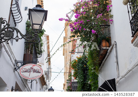 Charming Altea street showcases whitewashed buildings adorned with vibrant bougainvillea, a classic street lamp, and inviting eateries, perfect for Spanish family holidays Charming Altea street showcases whitewashed buildings adorned with vibrant bougainvillea, a classic street lamp, and inviting eateries, perfect for Spanish family holidays 143528387
