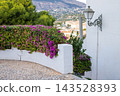 Cobblestone path with a traditional street lamp and purple bougainvillea on a white wall in Altea, Spain, offering beautiful views for travelers enjoying holidays 143528393
