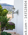 Charming Altea street scene with ornate lamp, vibrant bougainvillea, traditional houses, and scenic mountains under a clear Spanish sky during a family vacation 143528404