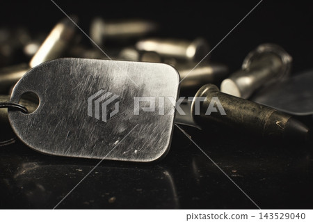 Close-up view of metal dog tags and bullets on a dark surface Close-up view of metal dog tags and bullets on a dark surface 143529040