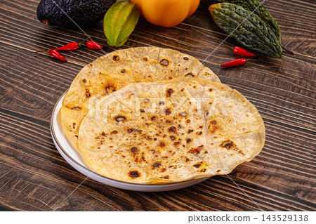 Freshly toasted flatbreads with charred golden spots stacked on white plate surrounded by avocado, peppers and chillies on rustic wood, healthy homemade food 143529138