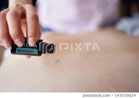 Female practitioner applying essential oil from a bottle onto the abdomen of a client, promoting relaxation and wellness in a serene environment with soft lighting and calming atmosphere Female practitioner applying essential oil from a bottle onto the abdomen of a client, promoting relaxation and wellness in a serene environment with soft lighting and calming atmosphere 143530024